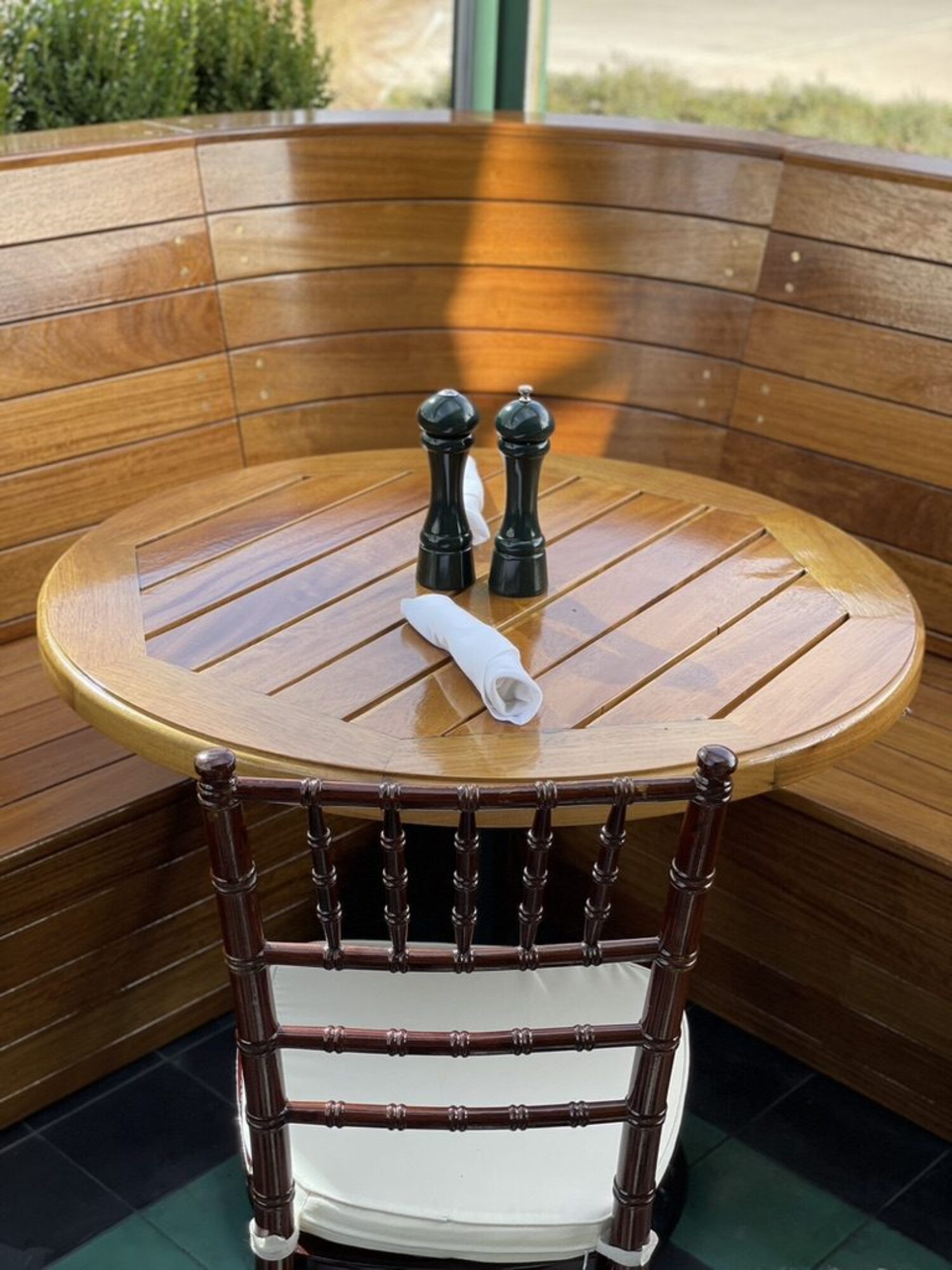 A wooden round tabletop with salt and pepper shakers, set in front of a curved wooden bench and a single wooden chair.