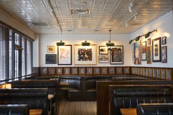 Elegant restaurant interior featuring rows of black leather booths, framed art on the walls, and green overhead lighting, creating a modern yet classic dining ambiance.