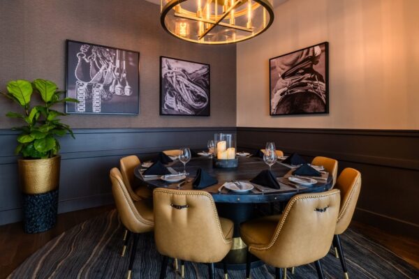 Intimate dining area at South Loft with a round table, leather chairs, and black-and-white wall art under a warm chandelier.