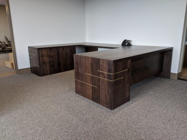 L-shaped dark wooden executive desk with brass inlay accents in a professional office setting.
