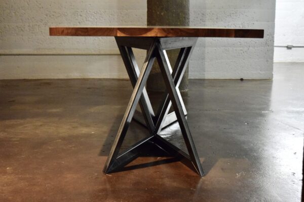 Handcrafted table by South Loft with a geometric metal base and thick wooden tabletop, placed in an industrial setting.