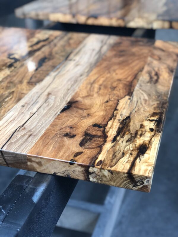 A close-up view of a polished wooden tabletop with unique natural patterns and rich textures in various shades of brown and cream.