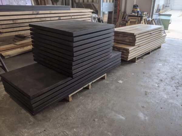 Stacks of dark and light wood tabletops are neatly arranged on pallets in a workshop, ready for further processing or installation.