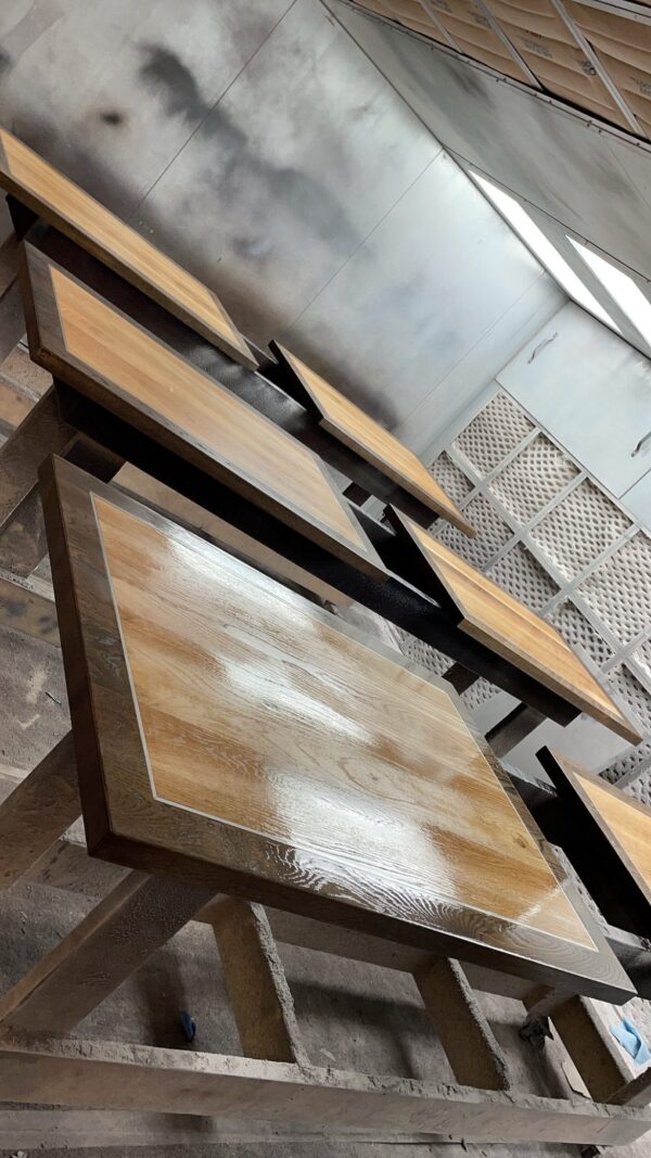 Multiple freshly stained wooden tabletops are placed in a workshop for drying, with a glossy finish reflecting light.