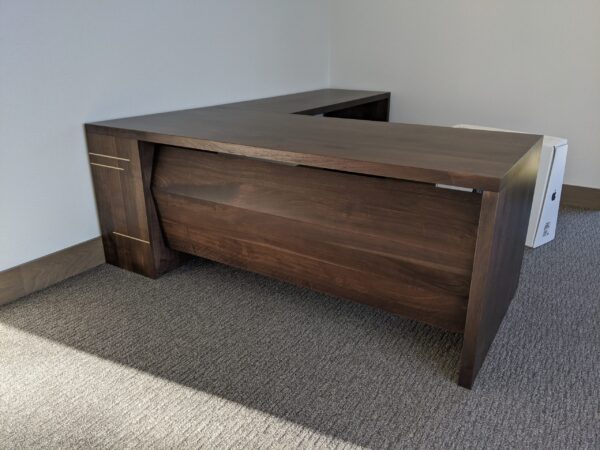 A modern dark wooden executive desk with brass inlay accents in a minimalistic office setup.