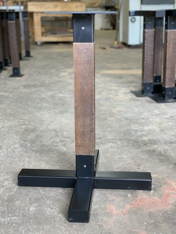 Close-up of a custom table leg with a textured wood finish and black metal base in the South Loft workshop, showcasing a blend of rustic and industrial design elements.