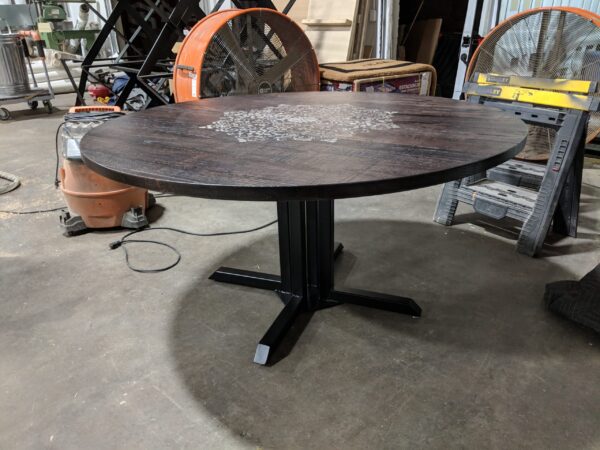Round wooden table with a dark-stained finish and intricate engraving on the tabletop, supported by a black metal base, created by South Loft in their workshop.