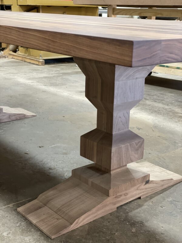 Custom walnut table with a geometric pedestal base and thick wooden top, showcasing craftsmanship by South Loft in a workshop setting.