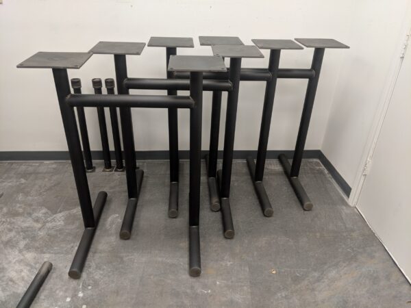 Collection of black cylindrical metal table legs designed by South Loft, arranged in a workshop, ready for assembly with a minimalist and industrial aesthetic.