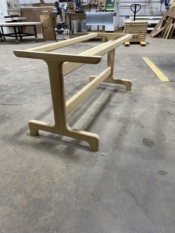 Handcrafted wooden table base with a natural finish, designed by South Loft, featuring rounded edges and clean, elegant lines, set in a workshop.