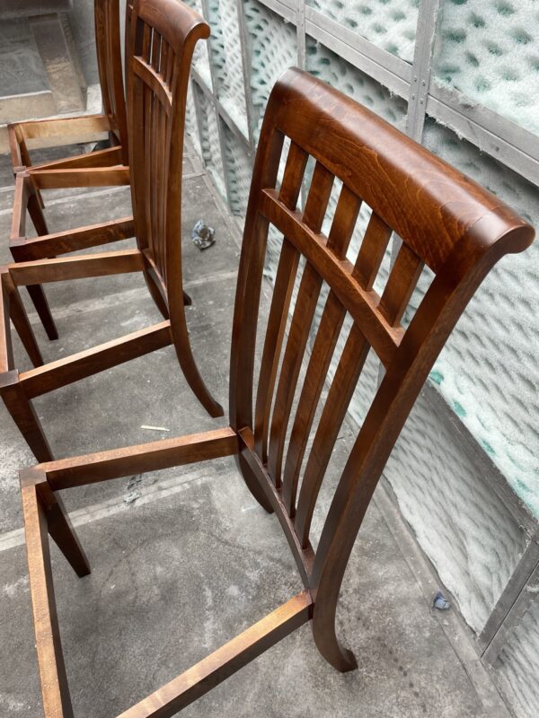 Row of handcrafted wooden chairs with curved backrests and vertical slats, made by South Loft, shown in a workshop setting.