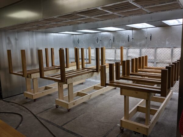Wooden table frames by South Loft, positioned upside down in a spray booth for finishing, displayed on a workbench in a controlled environment.