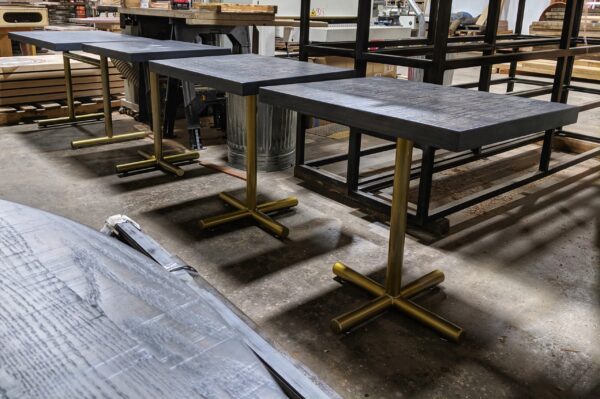 Rectangular tables by South Loft with dark wooden tops and gold-tone metal bases, displayed in a workshop.