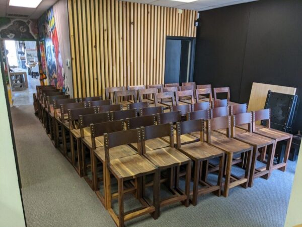 Rows of custom wooden chairs with leather backrests, designed by South Loft, neatly arranged in a workshop space with graffiti artwork on the walls.