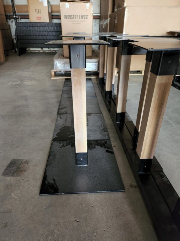 Wooden table legs attached to black metal bases lined up on the floor in the South Loft workshop, with labeled boxes in the background.