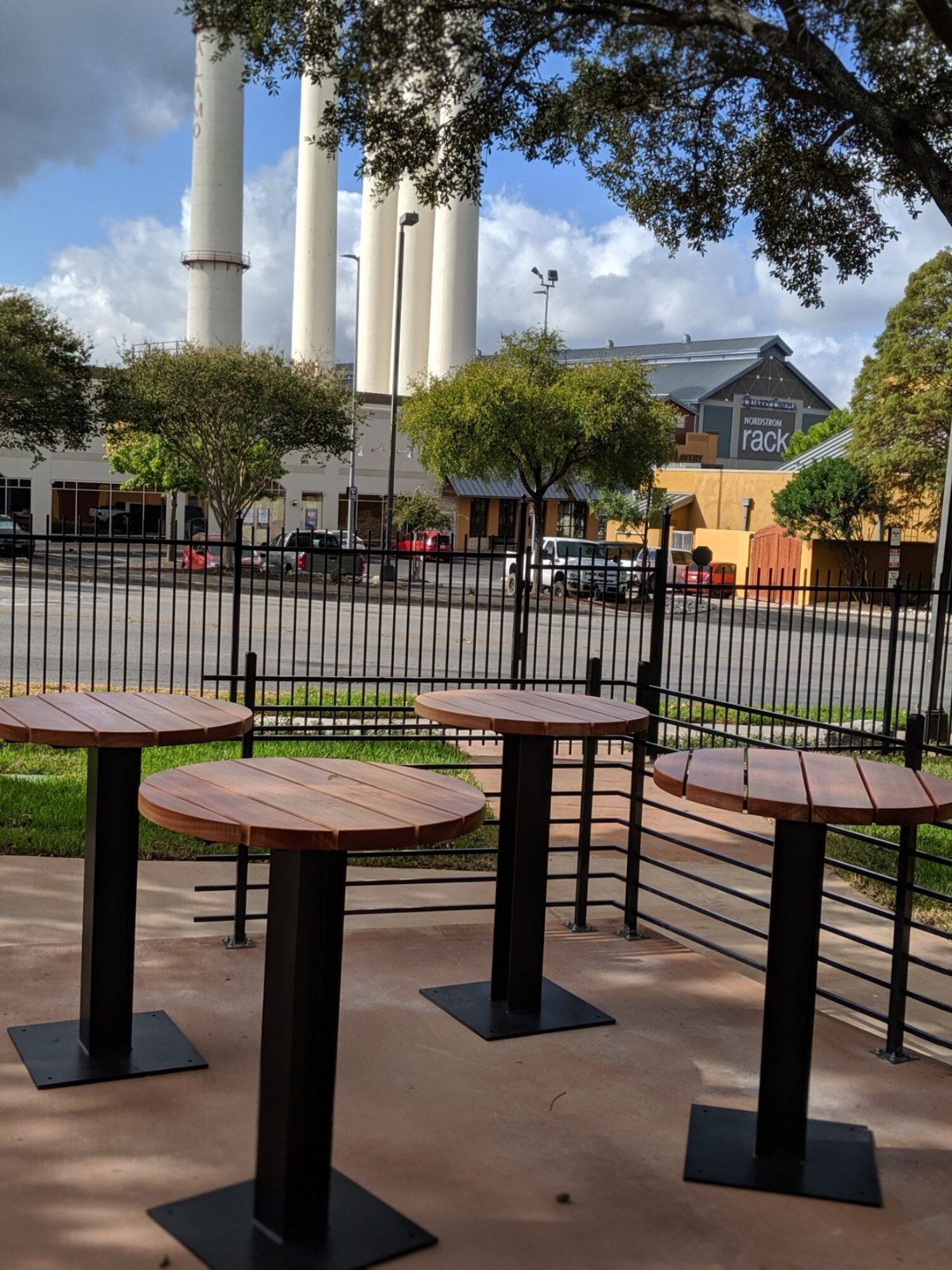 A group of 120 Series round tabletops with metal bases sit on a patio of a restaurant in urban environment.