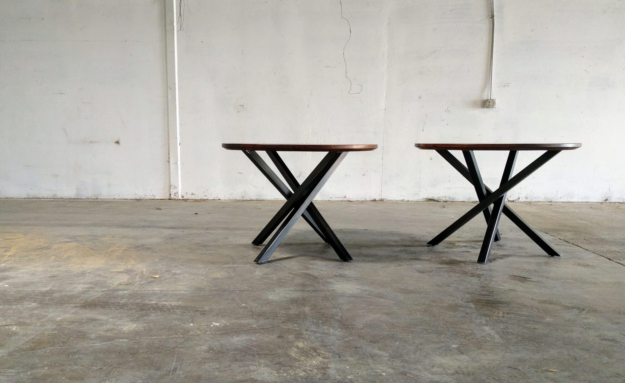 Two modern SouthLoft tables with wooden tops and black metal crisscross legs placed in an industrial space.