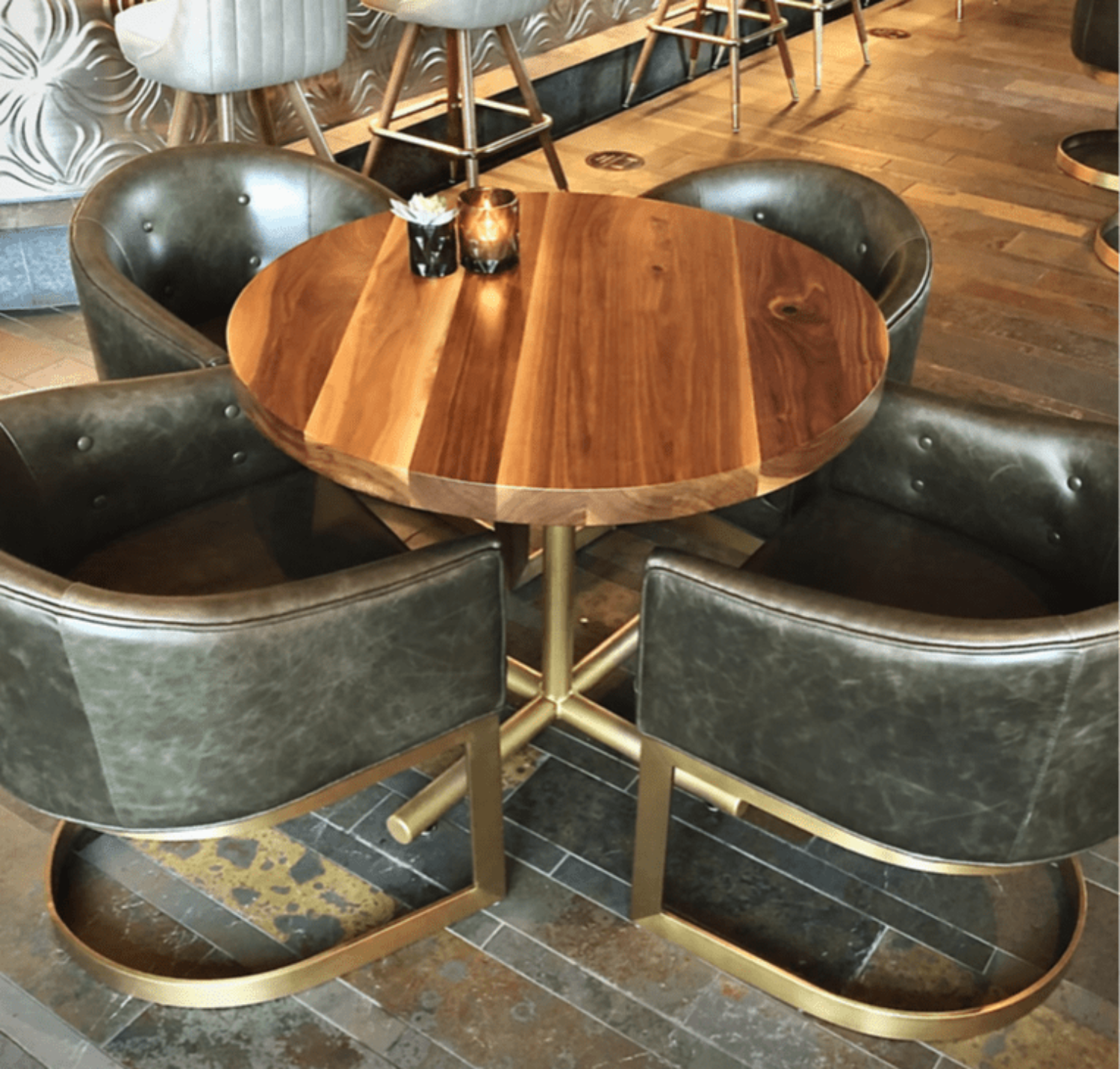 A round, custom wooden table with a smooth, natural wood grain finish, surrounded by four modern leather chairs with gold frames, showcasing South Loft's bespoke furniture design.