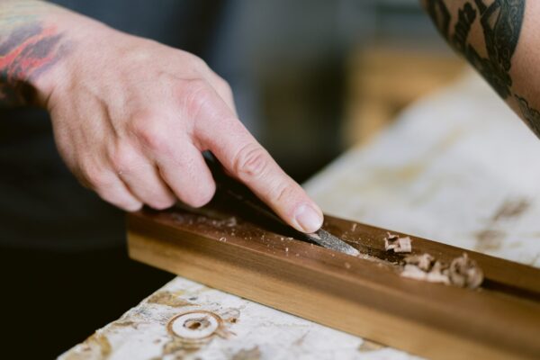 South Loft craftsman carving fine details into wood using a hand tool, showcasing precision and craftsmanship in custom furniture creation.