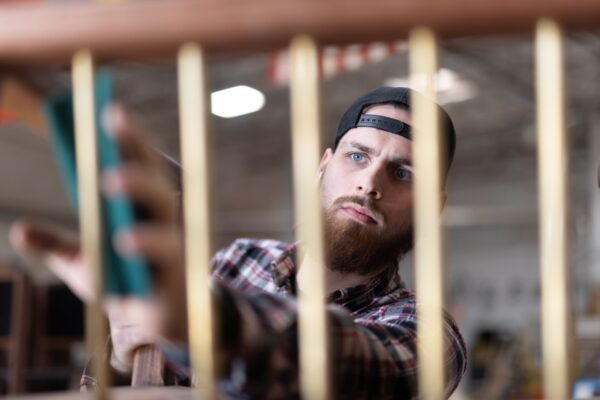 A focused craftsman at South Loft sanding a piece of custom furniture, wearing a plaid shirt and a backwards cap, emphasizing South Loft’s attention to detail and high-quality craftsmanship.