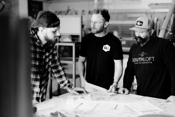 South Loft team members discussing design plans at a worktable, showcasing collaboration in custom furniture craftsmanship.