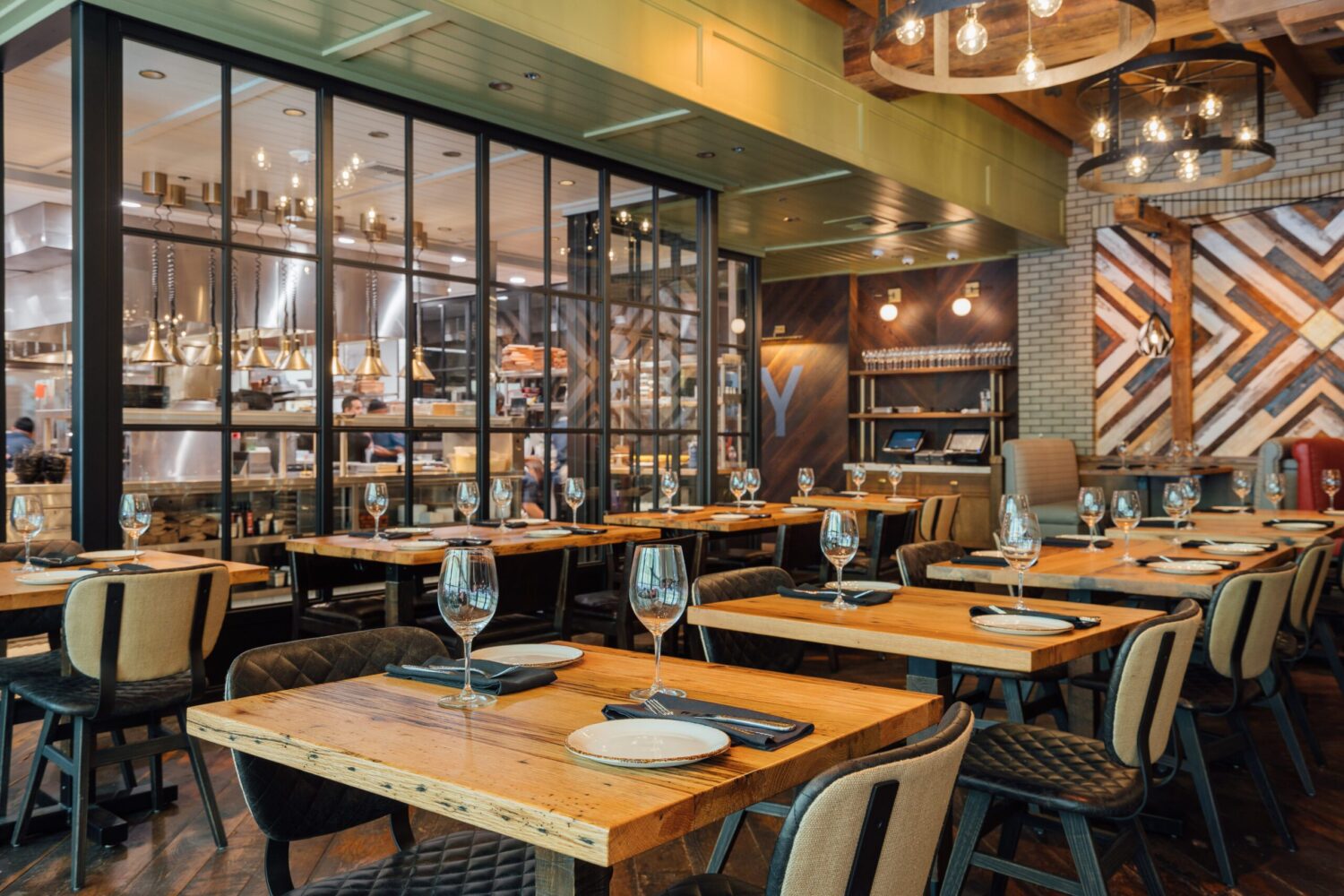 SouthLoft custom wooden tables and upholstered chairs in a modern restaurant with an open kitchen.
