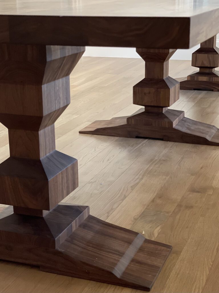 A close-up view of the pedestal legs of a custom walnut dining table by South Loft, showcasing the intricate geometric design and craftsmanship.