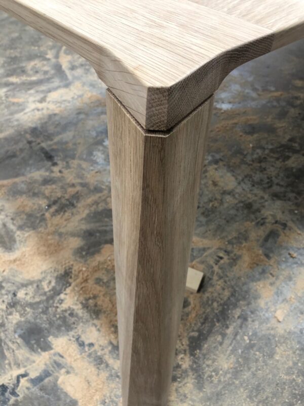 Close-up of a handcrafted oak table leg showcasing detailed joinery work with a lightly sanded finish.