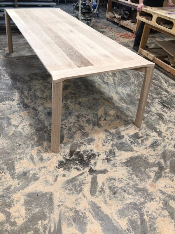 Unfinished handcrafted oak table surrounded by sawdust in a woodworking workshop.