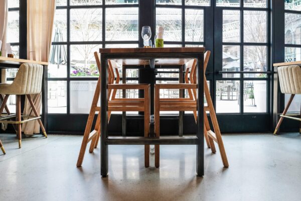 A modern dining setup featuring a sleek wooden table and chairs with metal accents, placed in front of large windows offering a view of the outdoor patio. The furniture was custom-designed by South Loft.