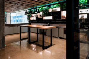 A sleek kitchen space with a custom wooden rectangular tabletop on black metal legs, surrounded by modern cabinetry and a lush green wall in the background. The table is designed by South Loft.