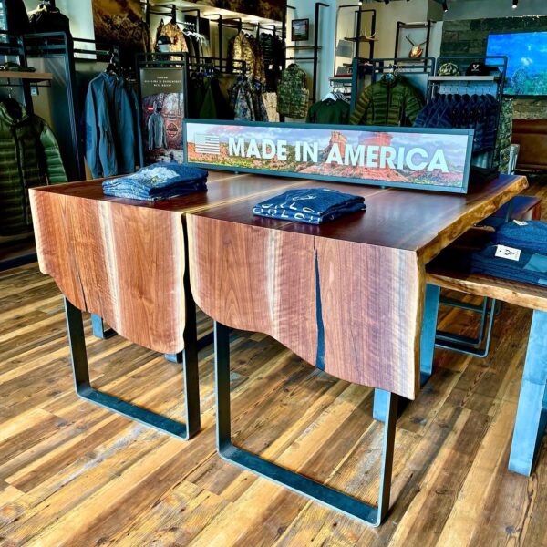 A pair of live-edge wooden tables with black metal legs are displayed in a retail store, with a 