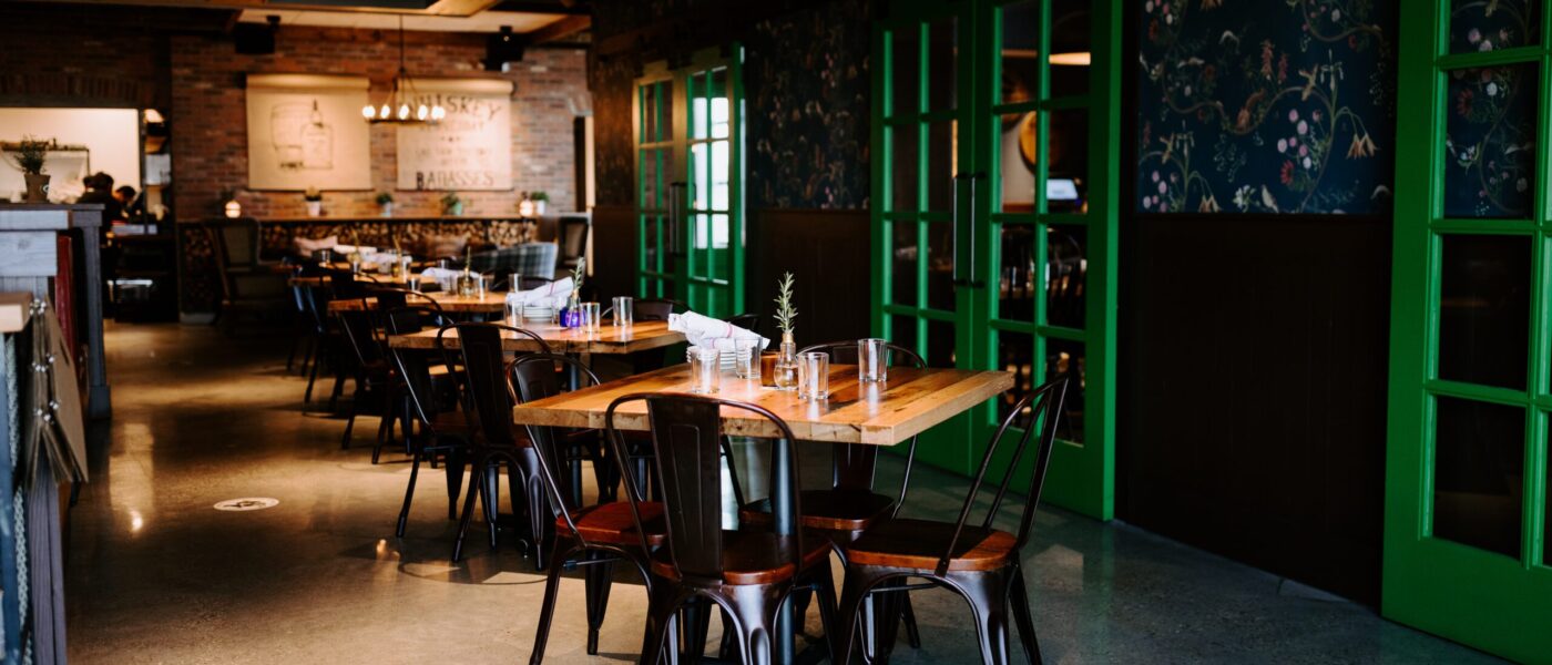 A cozy restaurant interior with wooden tables and metal chairs designed by South Loft, featuring vibrant green French doors and soft lighting for an inviting atmosphere.