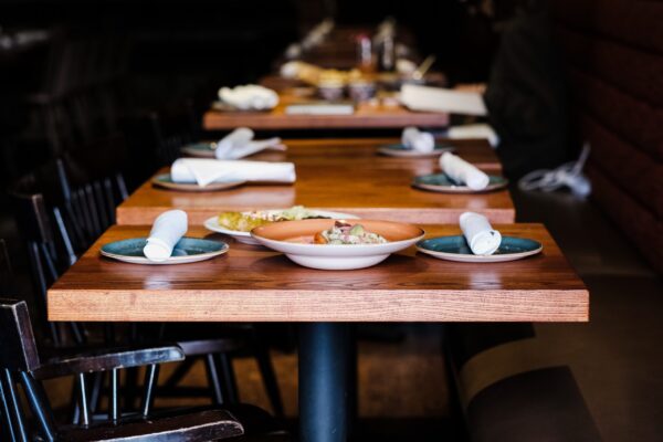 A close-up view of a wooden restaurant table, custom-made by South Loft, set with rolled napkins and teal plates, creating a welcoming dining environment with a focus on high-quality craftsmanship.