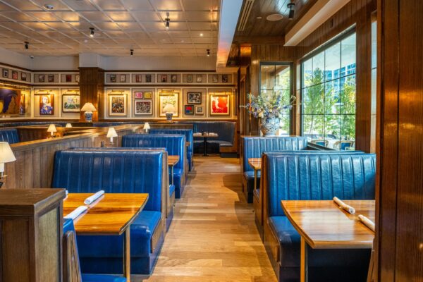 A stylish restaurant interior featuring blue leather booths and custom wooden tables by South Loft, with framed artwork lining the walls, creating a cozy and vibrant dining atmosphere.