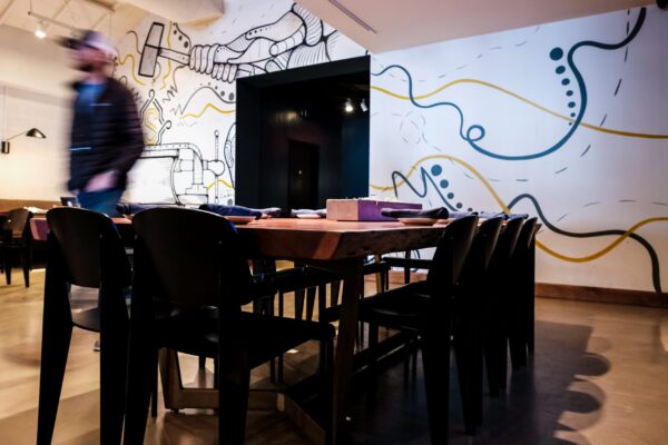 A modern restaurant setting featuring a custom wooden table crafted by South Loft, surrounded by black chairs, with a vibrant wall mural in the background.