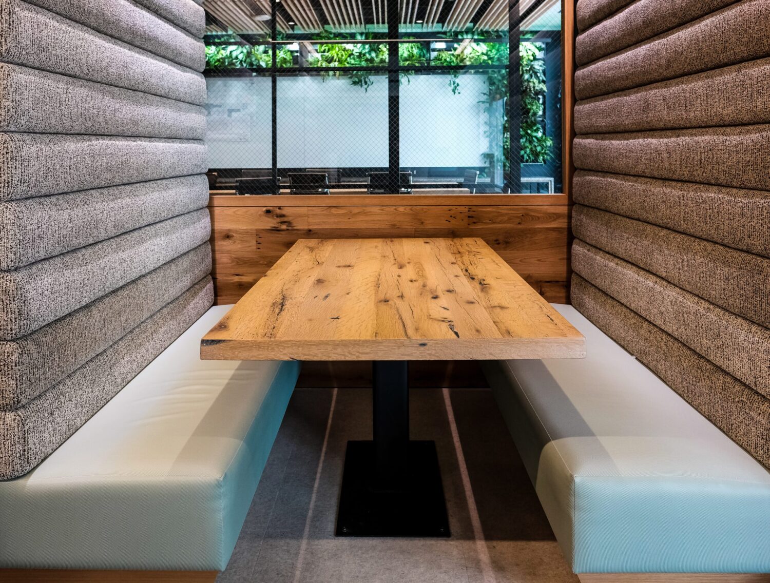 SouthLoft custom wooden rectangular tabletop with rustic wood grain and knots, set in a cozy booth with padded gray fabric and pale blue cushions in a modern restaurant.
