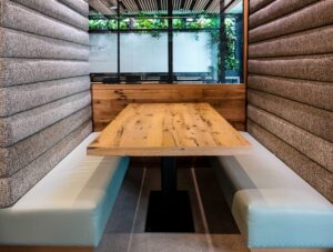 SouthLoft custom wooden rectangular tabletop with rustic wood grain and knots, set in a cozy booth with padded gray fabric and pale blue cushions in a modern restaurant.