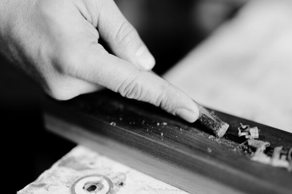 A close-up of a woodworker’s hand delicately carving wood, showcasing South Loft’s dedication to fine craftsmanship and attention to detail.
