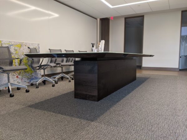 A modern, sleek conference table by South Loft, crafted in dark wood, set in a well-lit office meeting room, symbolizing South Loft's commitment to combining style and functionality.