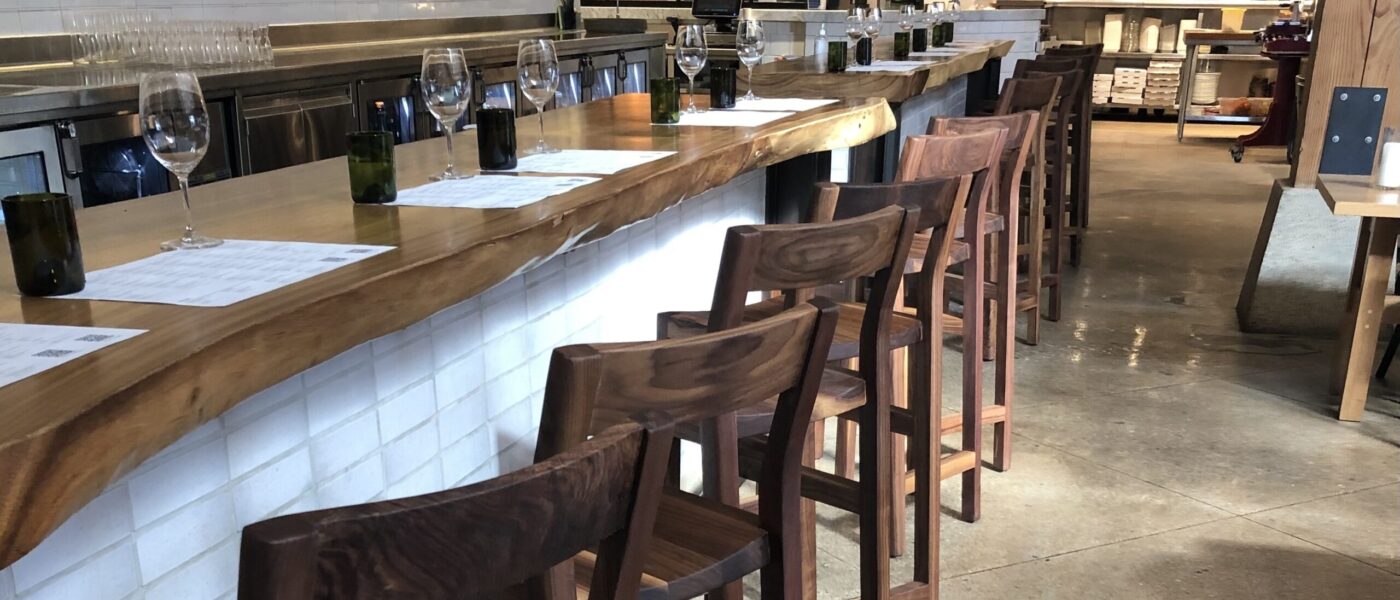 A bar seating area with handcrafted wooden stools and a live-edge wood counter designed by South Loft, in a modern restaurant setting.