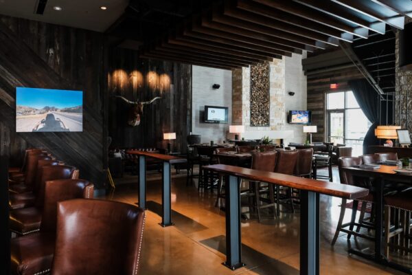 A modern dining space featuring leather chairs, wooden tables, and dark wood-paneled walls with a mounted longhorn head and artwork.