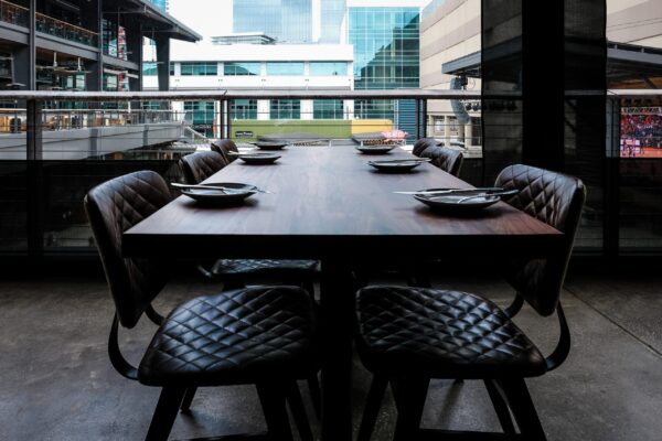 South Loft custom walnut dining table with quilted leather chairs on an outdoor balcony overlooking a modern cityscape.
