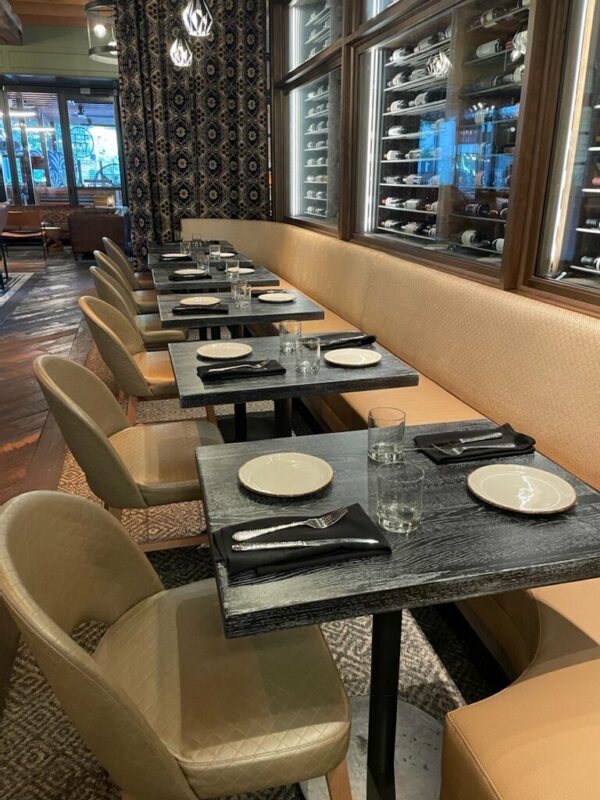 South Loft dining tables with beige cushioned seating in a modern restaurant with wine displays.