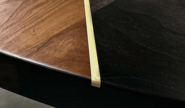 Close-up of a South Loft custom dining table corner showing a smooth walnut wood grain with a metallic trim.