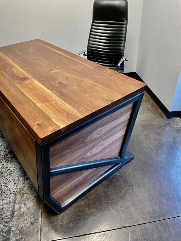 South Loft custom executive desk with dark wood grain top and black metal base, shown with a black ergonomic office chair in a minimalist office.
