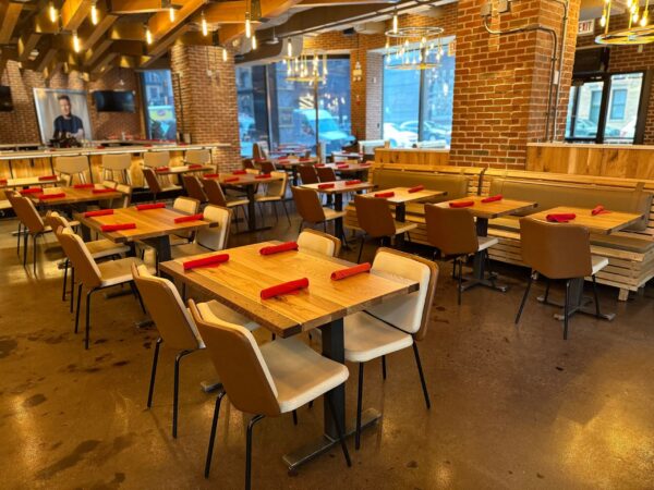 South Loft custom wood tables and chairs in a spacious restaurant, set with red napkins, featuring exposed brick walls and overhead lighting.