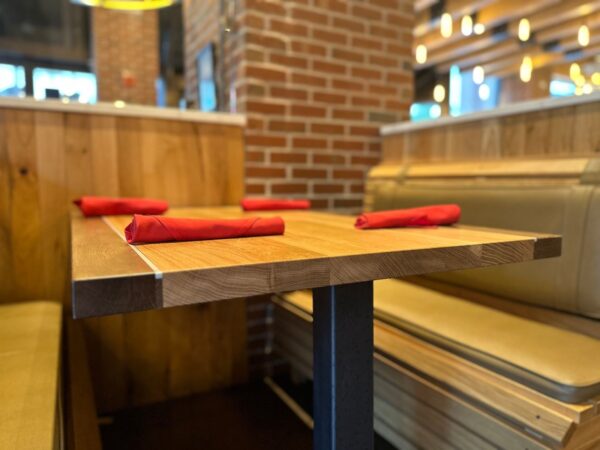 South Loft custom table with light wood finish, set with red napkins in a booth seating area featuring brick walls and soft lighting.
