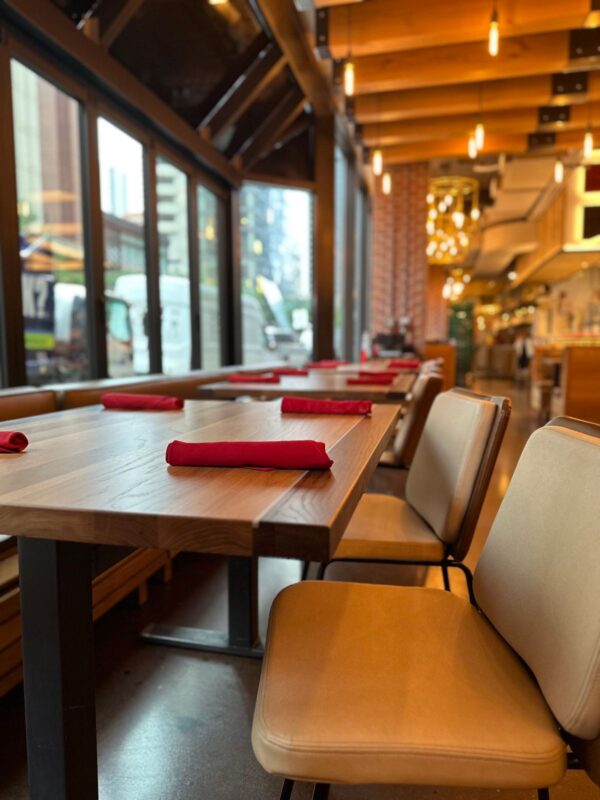 South Loft custom dining table and chairs with red napkins in a modern restaurant interior with large windows.