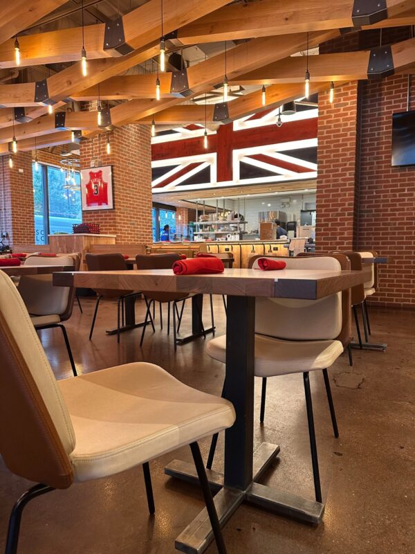 Modern restaurant interior with South Loft custom dining tables and chairs, featuring red napkins, wood beams, and a British Union Jack design in the kitchen area.